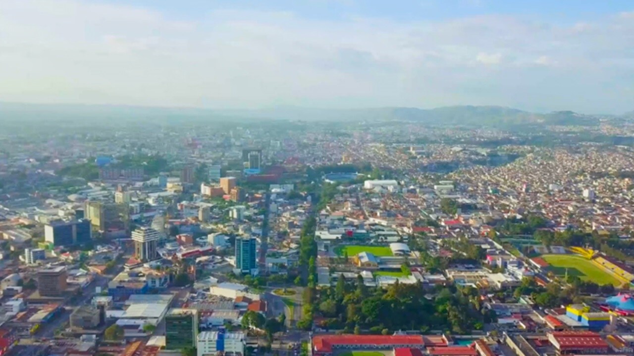 A vibrant cityscape with numerous buildings adjacent to a spacious green field, showcasing urban and natural elements.
