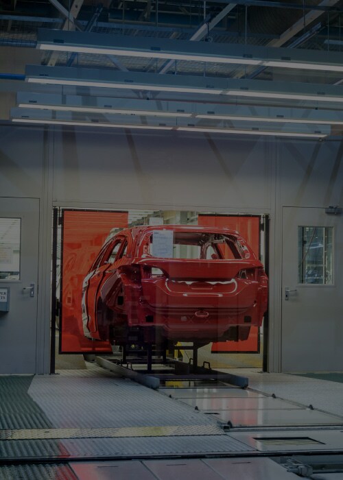 Red car body moving through an automated automotive manufacturing assembly line inside a factory.
