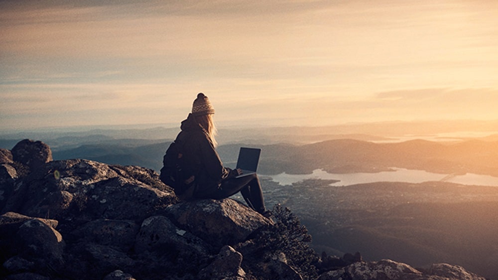 A woman efficiently manages digital delivery tasks while enjoying the serenity of the hills.