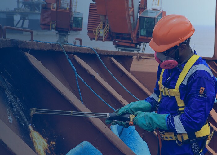 A man in blue shirt and orange safety gear working on a ship, ensuring safety and maintenance.