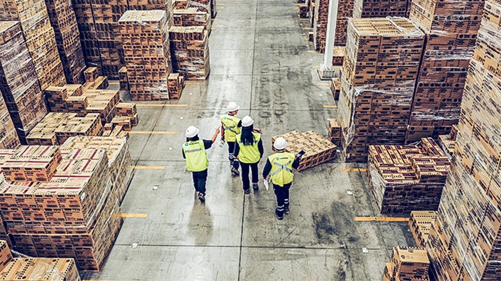 Warehouse team walking through a large storage facility with stacked pallets and boxes
