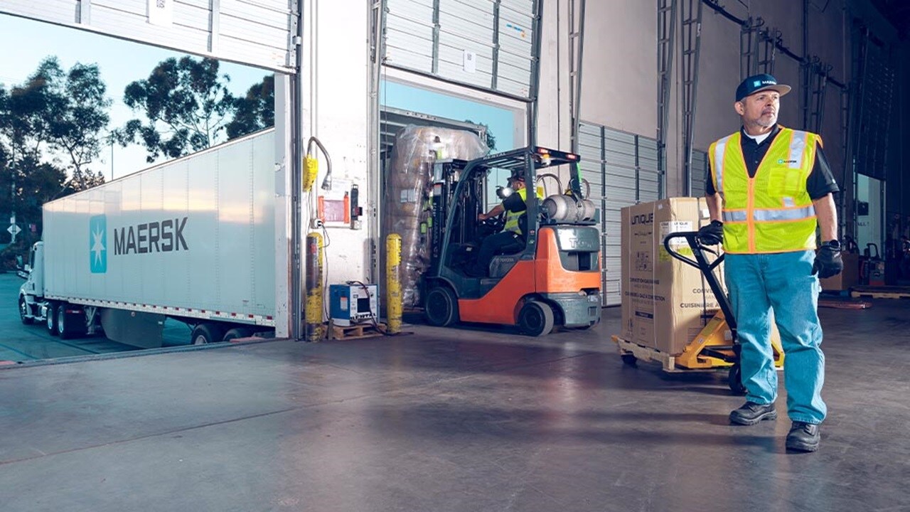 A man stands in front of a warehouse, next to a forklift.