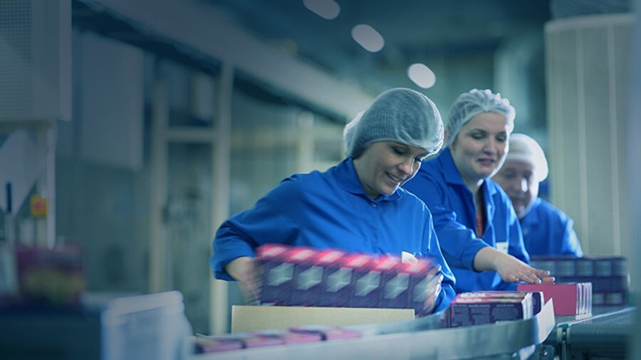A group of workers arranging FMCG items on a conveyor belt in a distribution centre.