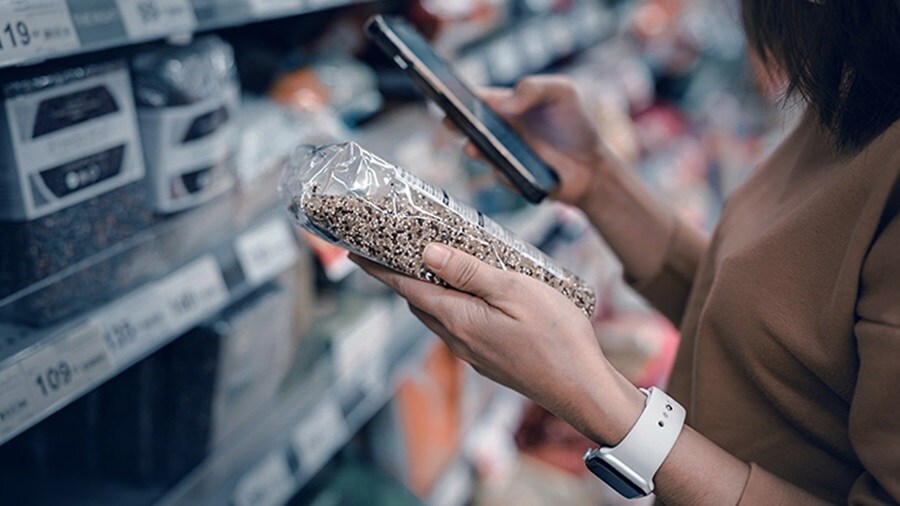 Close-up of a woman holding an FMCG product in their left hand and a mobile in the right hand.