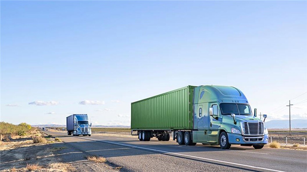 Two large trucks traveling down a highway.
