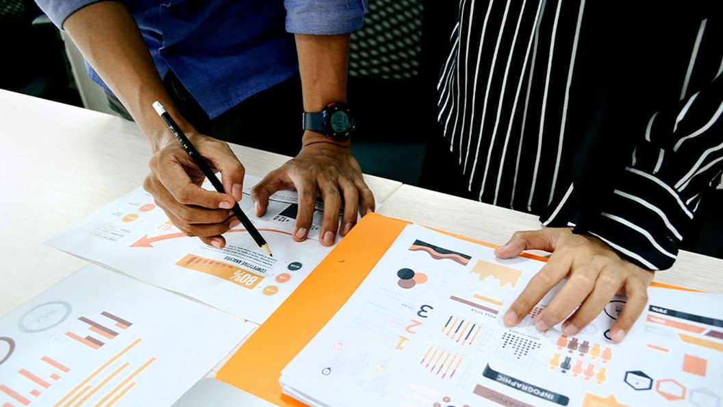 Two people collaborating on a document, using a pen and paper to take notes and share ideas.