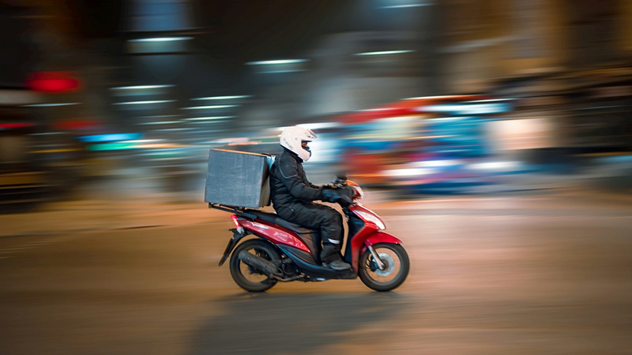 A Man riding delivery motorcycle on a road during daytime