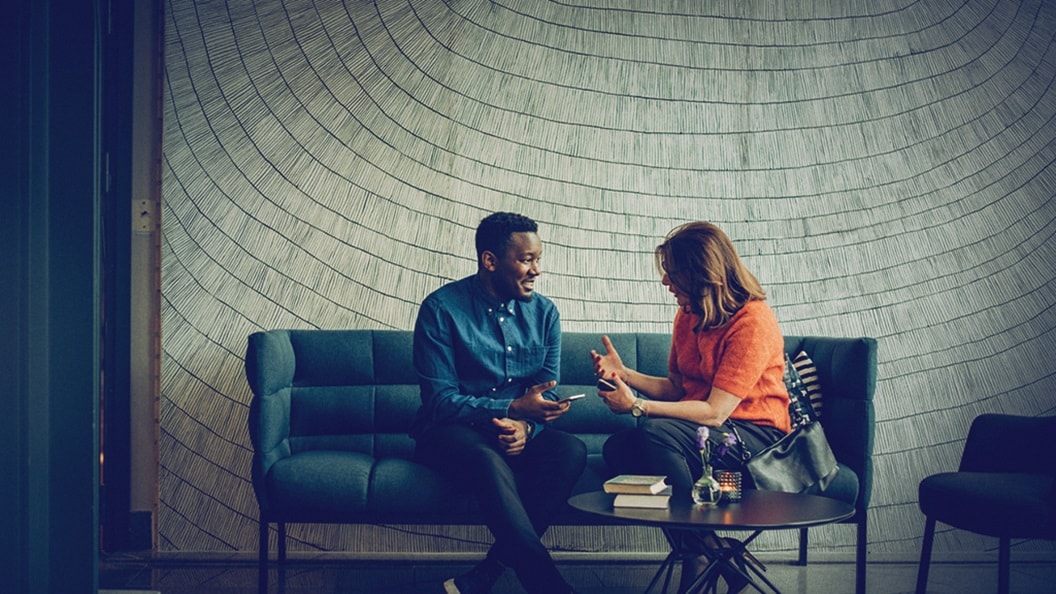 Customer supply chain management – A man and a woman, seated on a sofa, discussing in an office.