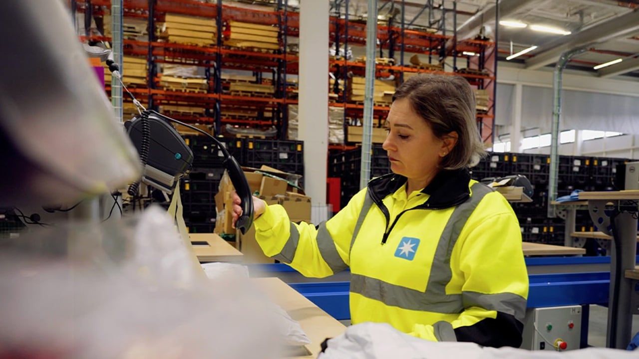 A woman in a safety vest is organizing items in a warehouse.