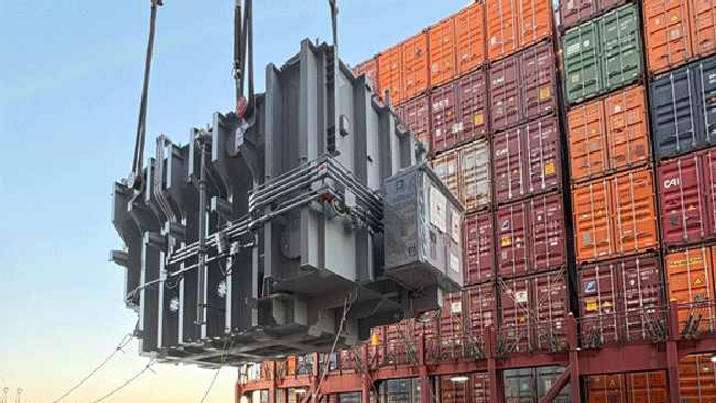 Transformer being lifted in front of shipping containers