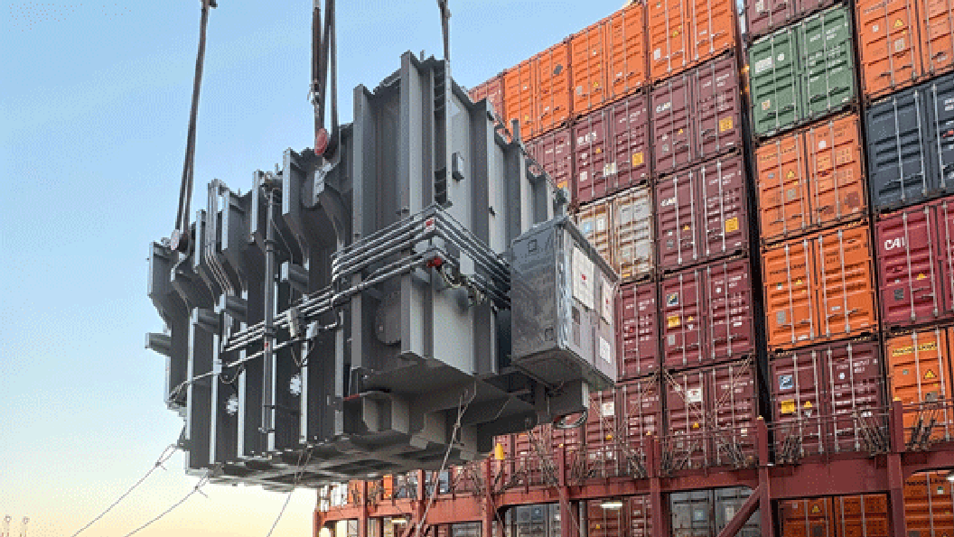 Transformer being lifted in front of shipping containers