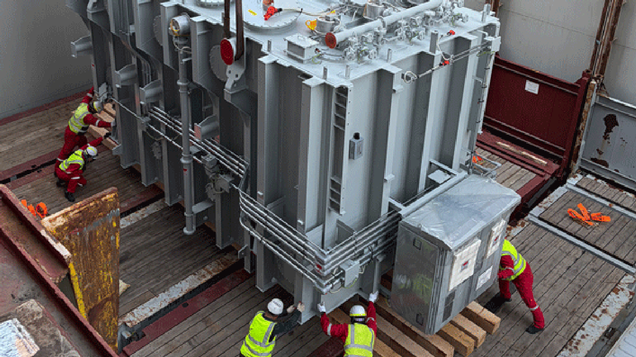 Transformer being positioned on a trailer by workers