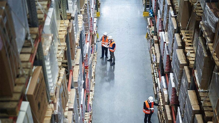 Employers holding digital tabs in retail warehouse full of shelves with goods.