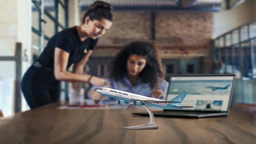 Two women working at a desk with a model airplane labeled 'Maersk Air Cargo' in the foreground.
