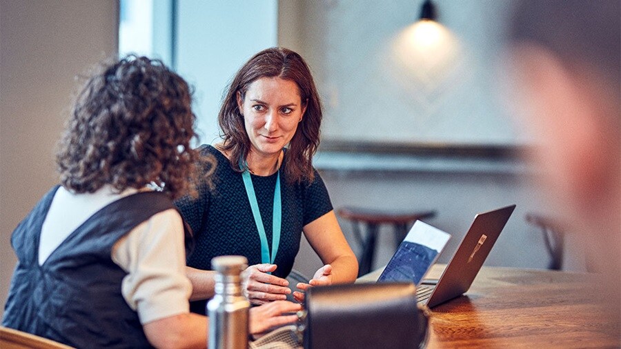 Three individuals in a meeting room, one holding a document, with faces obscured for privacy.