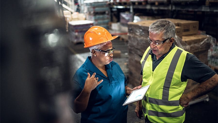 Two warehouse workers discussing data on a tablet in a storage facility.