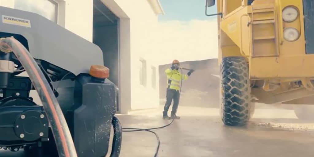 Worker power washing a large yellow truck.