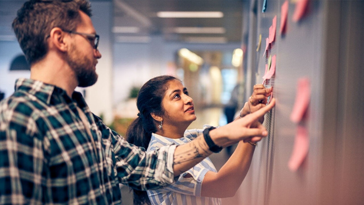 Two coworkers collaborating and placing sticky notes on a wall during a brainstorming session.