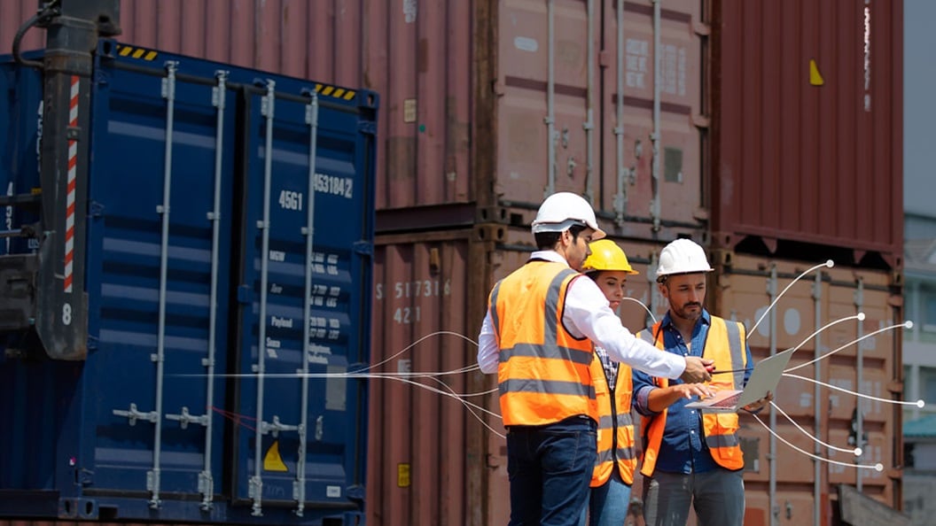 Three men in orange vests stand beside colorful shipping containers at a logistics yard.