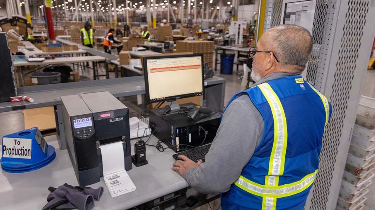 A man in a safety vest is focused on working at a computer in a professional setting.