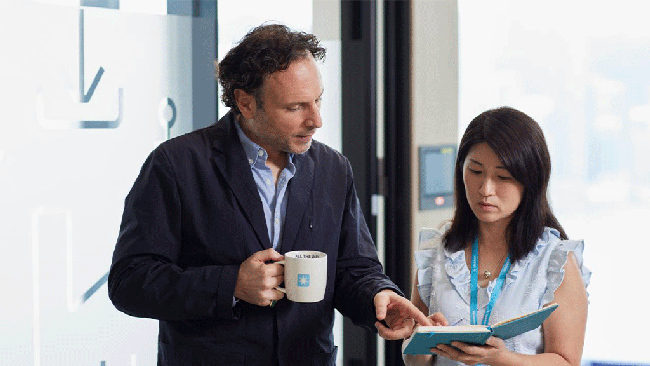  A man and woman stand together, smiling, in front of a large coffee cup on a table.