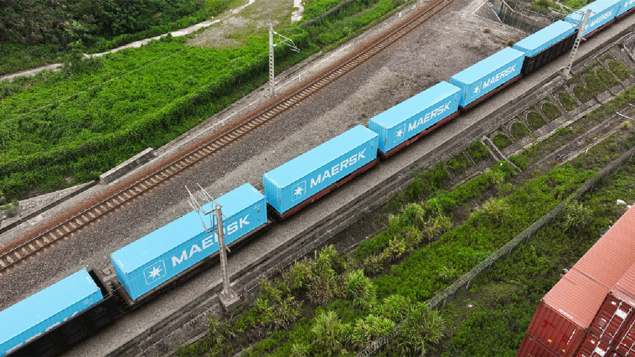 Aerial view of a blue train traveling along a railway track surrounded by greenery.