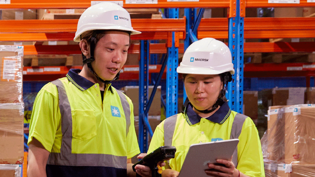 Two warehouse workers in safety helmets and high-visibility shirts.