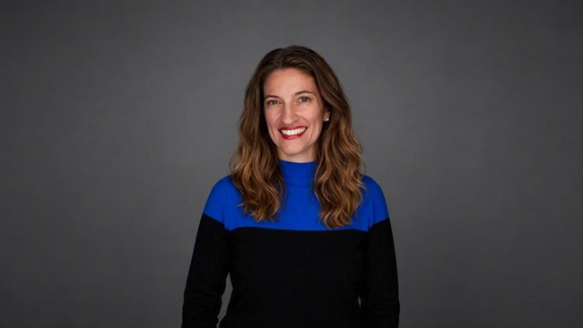 Portrait of a person in a blue and black top against a grey background.