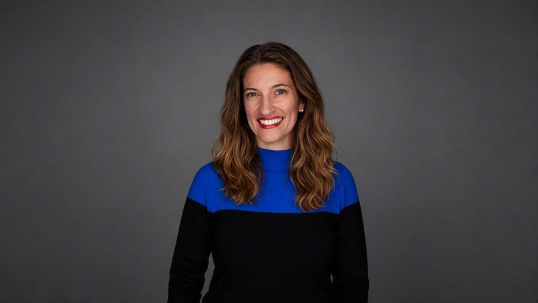 Portrait of a person in a blue and black top against a grey background.