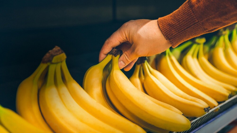 Hand selecting fresh bananas in a grocery store produce section