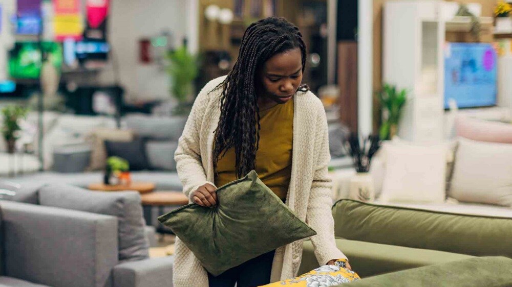 A woman standing in a store, thoughtfully looking at a couch on display.