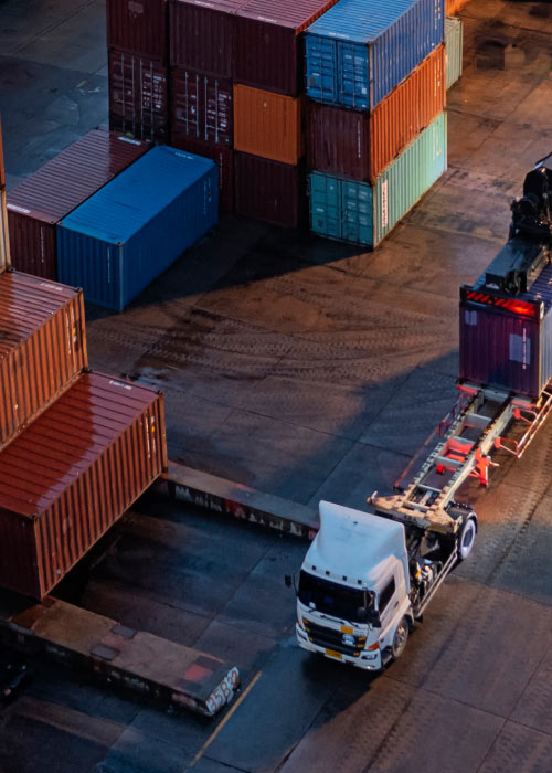 Shipping containers are stacked in an organised manner at a cargo port while a forklift is carrying a container.
