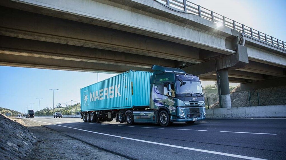 Maersk-branded container truck driving on a highway under an overpass, transporting a shipping container by road.
